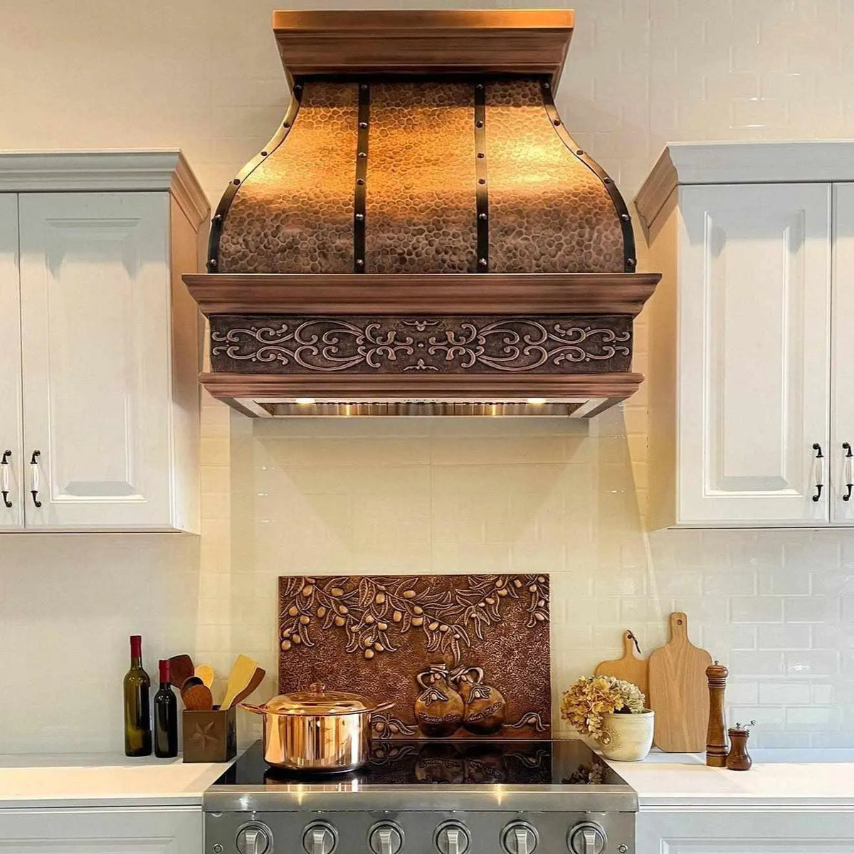 Antique copper range hood with a bell shape and straps, featuring an apron design, installed over a kitchen stove.