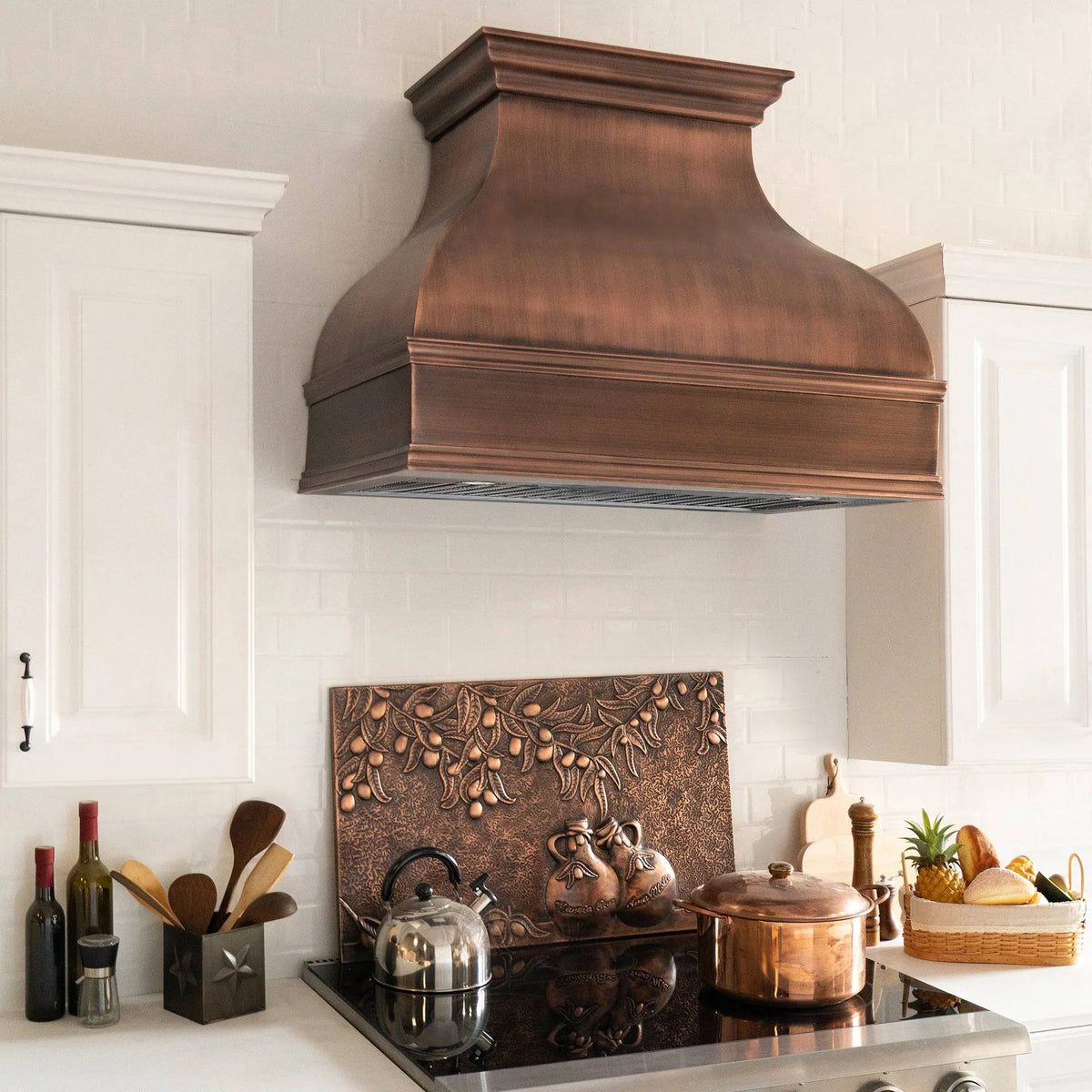 Antique copper range hood installed above a kitchen stove with a white tile wall in the background.