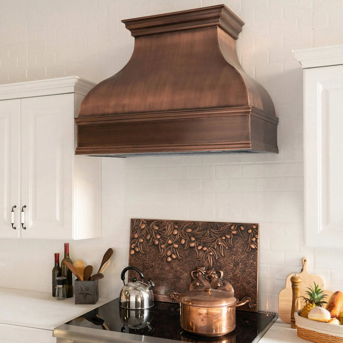 Antique copper range hood installed above a kitchen stove with a white tile wall in the background.