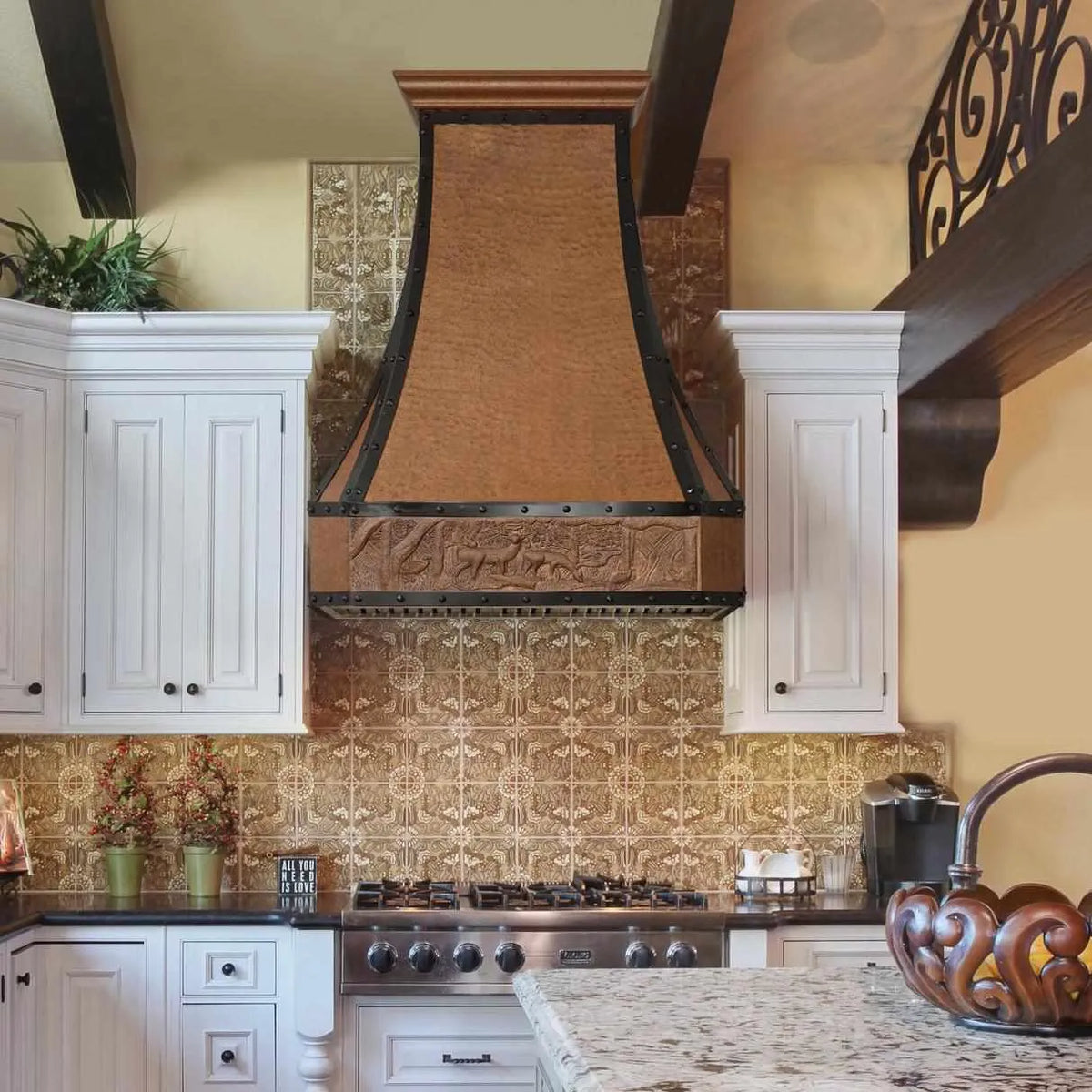 Retro copper range hood with deer apron pattern installed over a kitchen sink, featuring a beehive hammered texture.