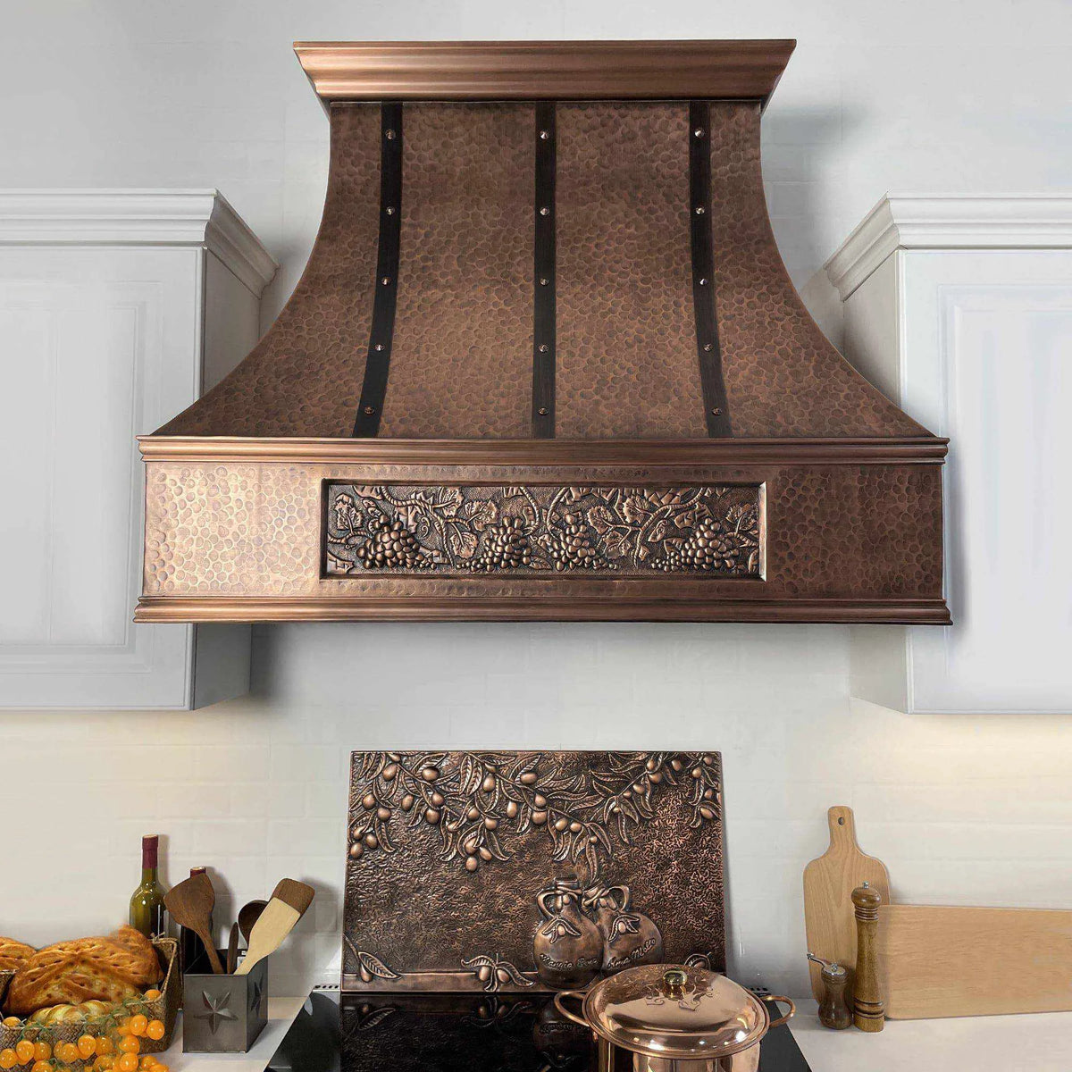 Antique copper range hood with a curved design and dark straps, featuring intricate patterns