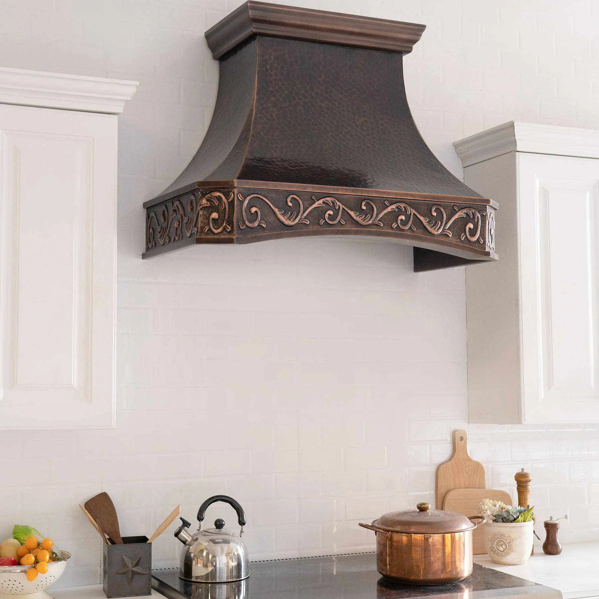Handmade dark antique copper range hood installed in a modern kitchen with white cabinets