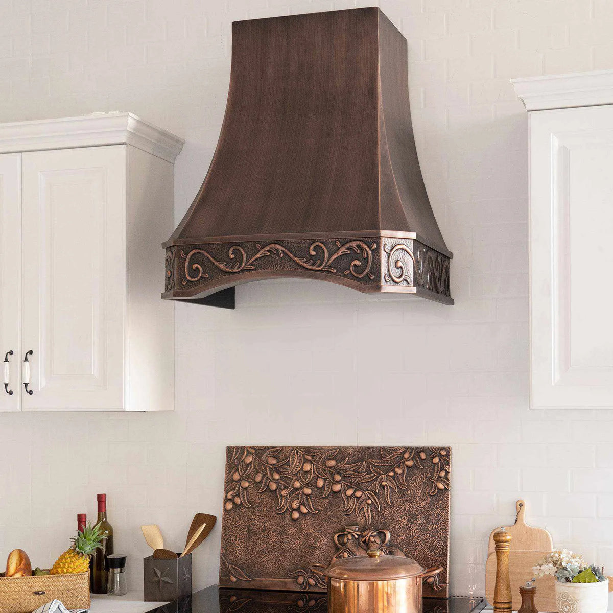 Antique copper range hood with intricate design, installed above a kitchen stove, with vintage apron pattern.