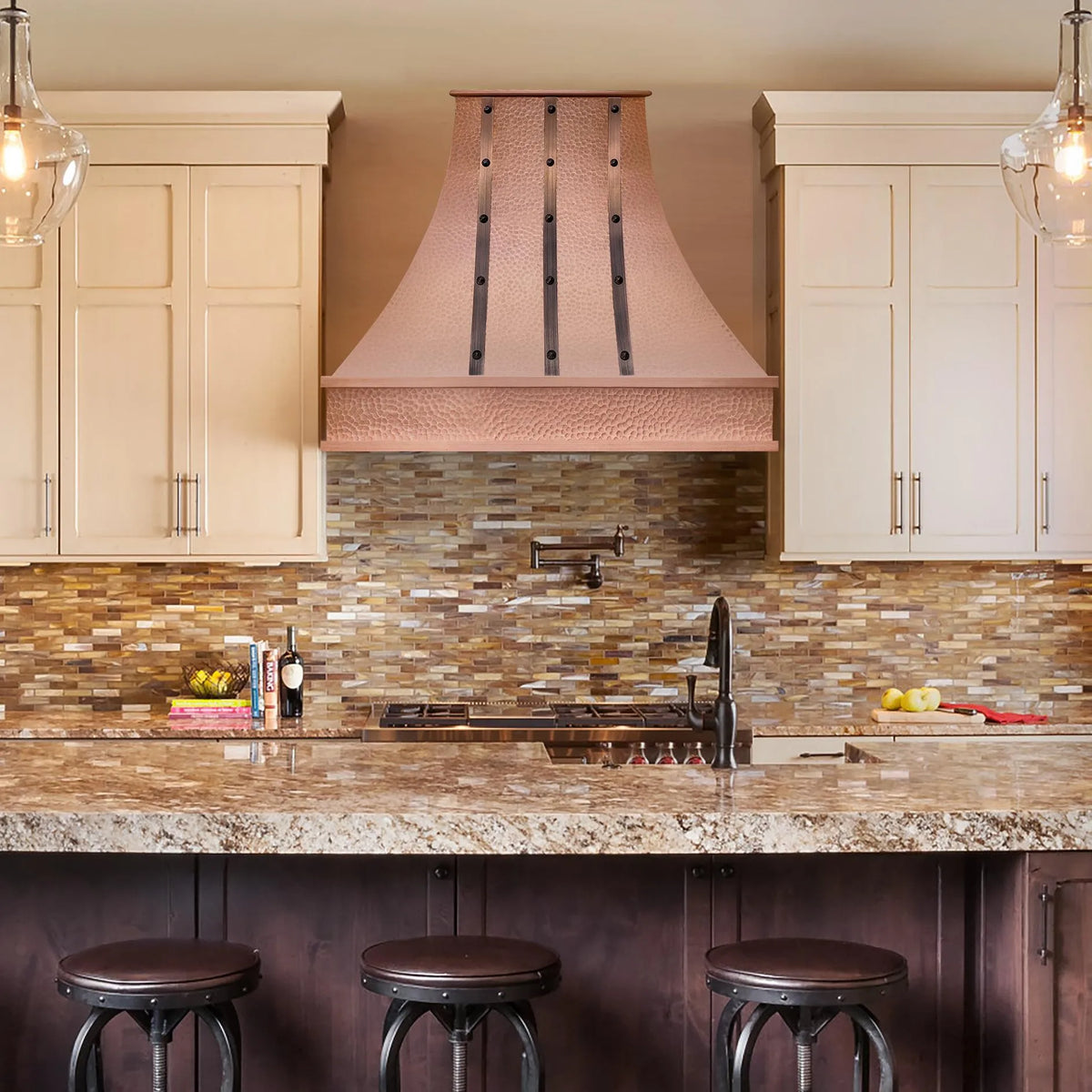 A natural copper range hood with a hammered texture installed above a kitchen sink and counter, with a matching copper apron.