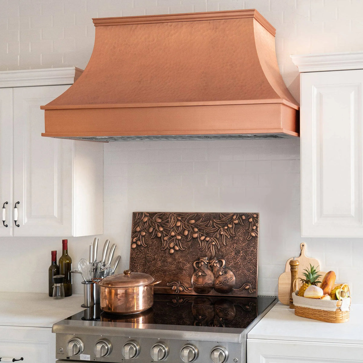 A natural copper range hood with a curved design, placed above a kitchen stove, with a copper backsplash and kitchen decor in the background.