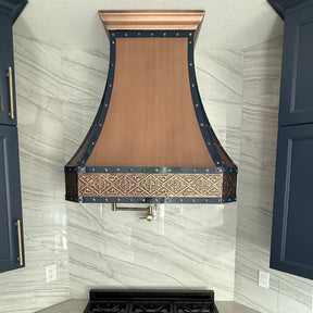 Decorative copper range hood mounted on a kitchen wall with marble backsplash.