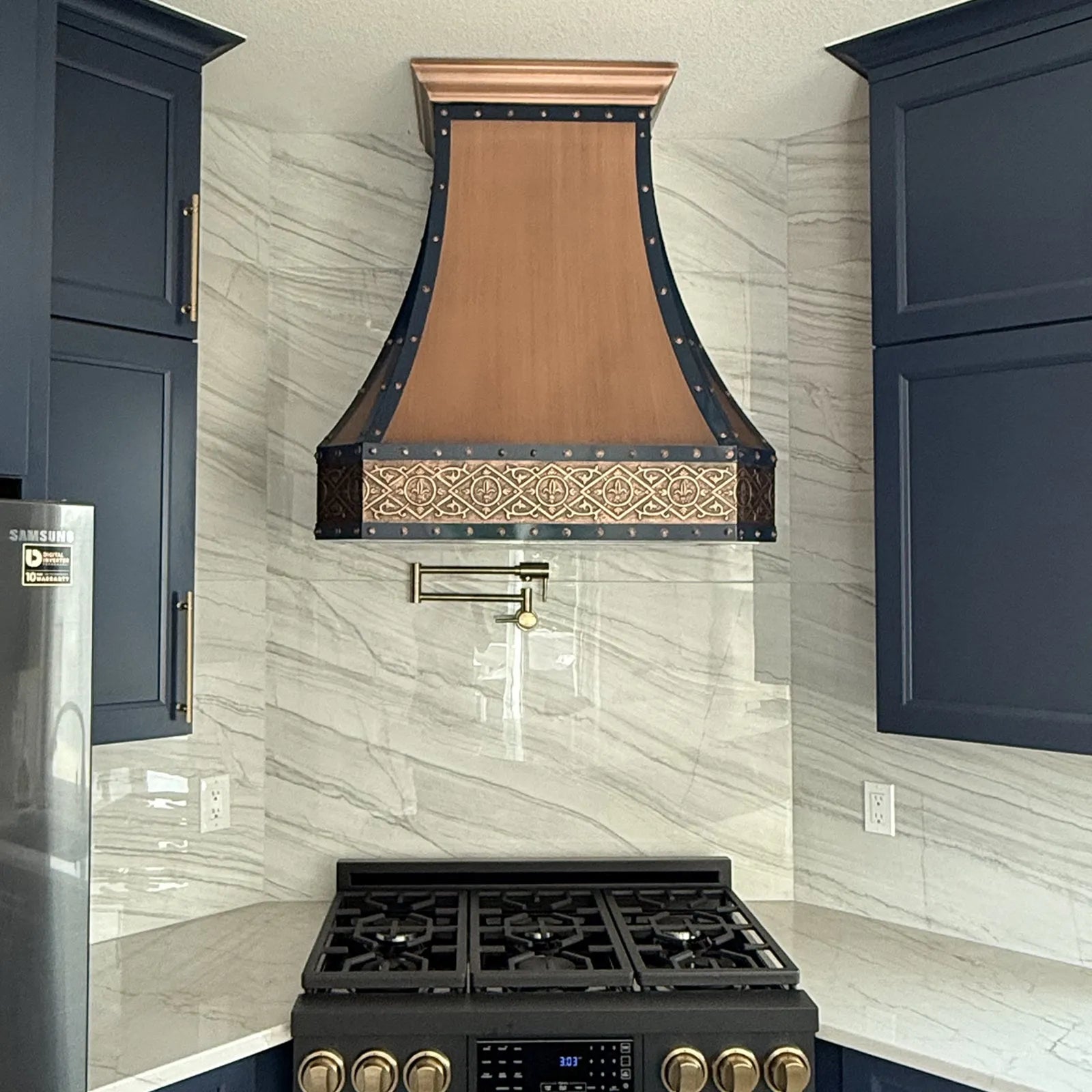 Kitchen with a copper range hood and black stove against a tiled wall.