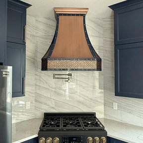 Kitchen with a copper range hood and black stove against a tiled wall.