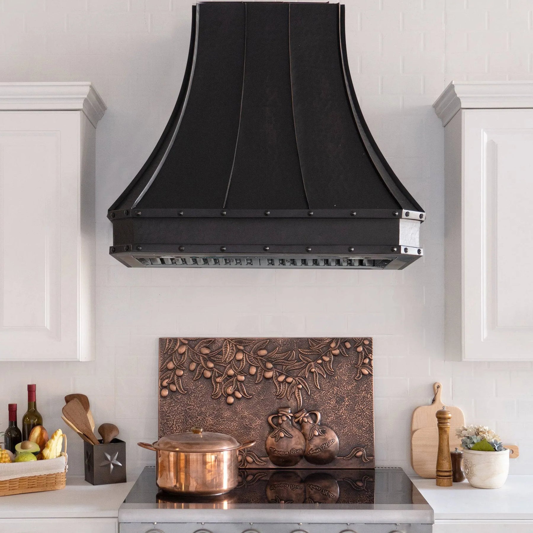 A bronze copper range hood with rivet details, displayed in a kitchen setting above a cooking area.