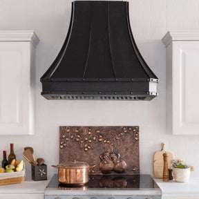 A bronze copper range hood with rivet details, displayed in a kitchen setting above a cooking area.