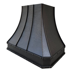 A bronze copper range hood with rivet details, displayed in a kitchen setting above a cooking area.