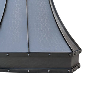 A bronze copper range hood with rivet details, displayed in a kitchen setting above a cooking area.