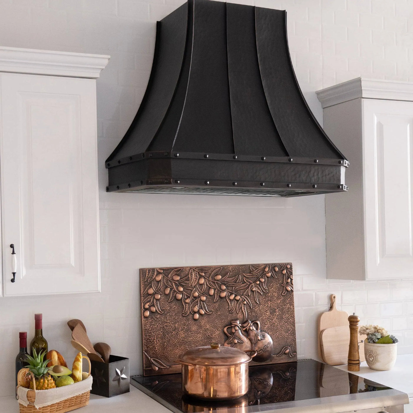 A bronze copper range hood with rivet details, displayed in a kitchen setting above a cooking area.