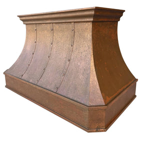 A handmade vintage copper range hood installed above a kitchen stovetop, featuring a curved design with rivets and straps.