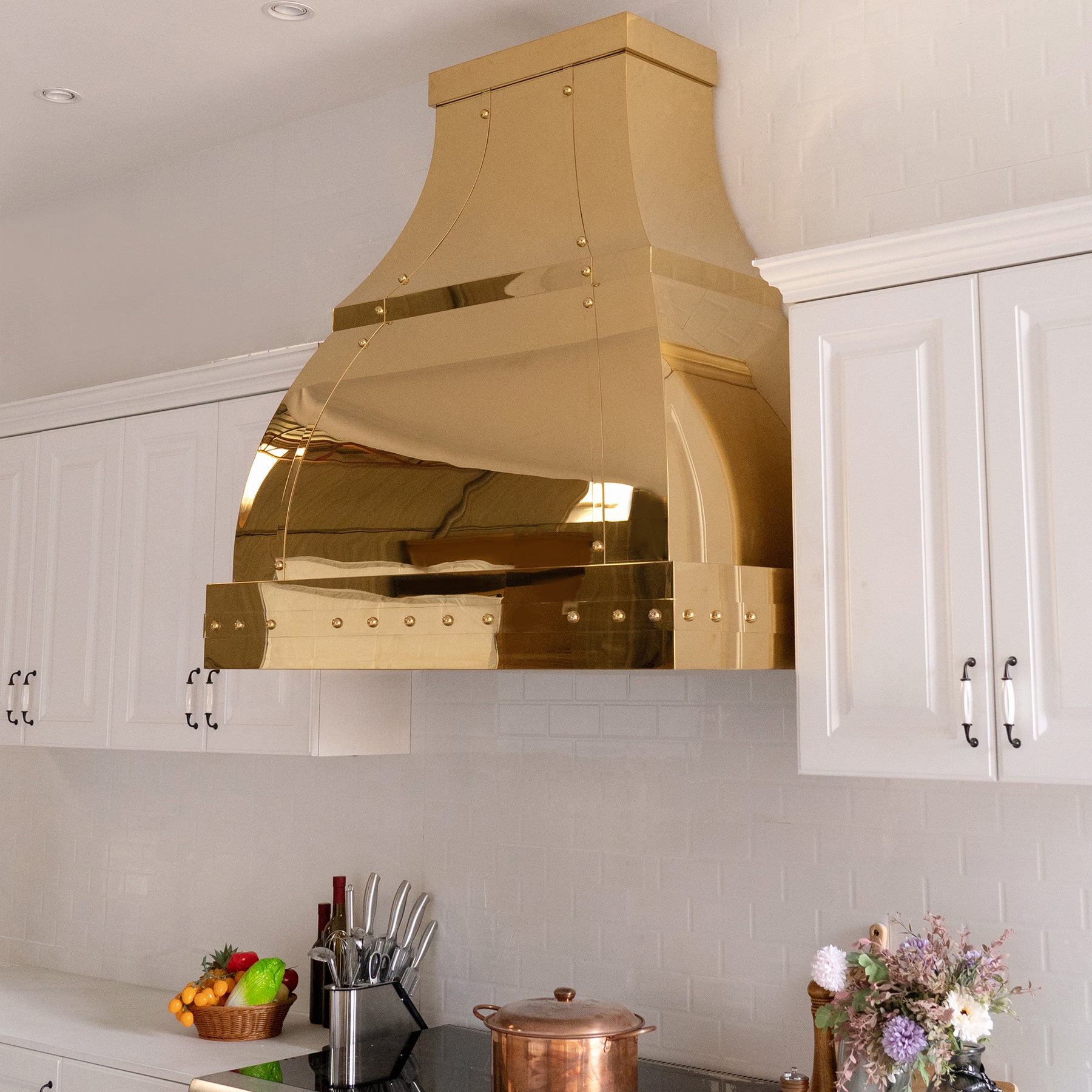 Fobest custom handmade polished brass range hood with brass straps and rivets installed in the white kitchen